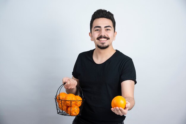 joven sosteniendo una canasta metálica llena de frutas naranjas.