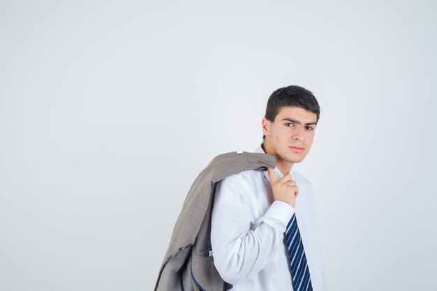 Joven sosteniendo la chaqueta sobre el hombro mientras posa con camisa blanca y corbata