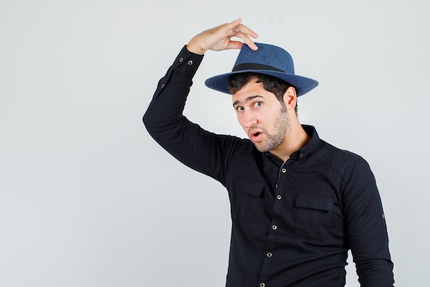 Foto gratuita joven sosteniendo los dedos en el sombrero de camisa negra