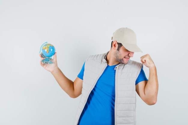 Foto gratuita joven sosteniendo el globo de la escuela en camiseta, chaqueta y mirando dichoso, vista frontal.