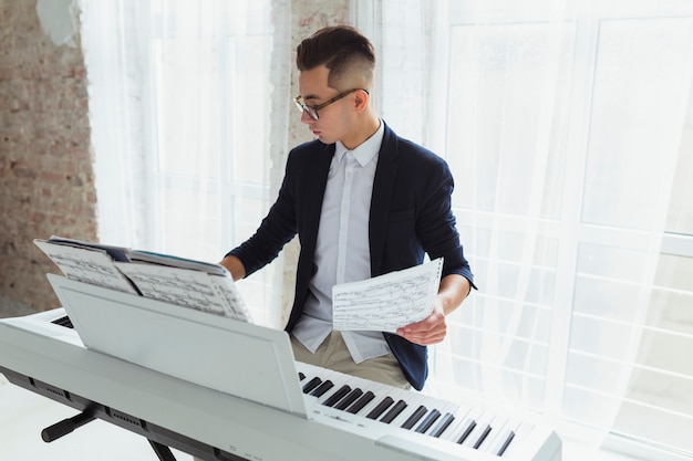 Joven sosteniendo una hoja musical tocando el piano sentado cerca de la ventana