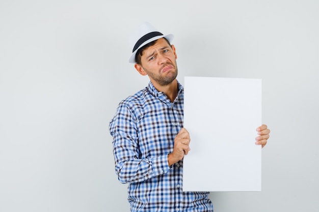 Foto gratuita joven sosteniendo lienzo vacío en camisa a cuadros