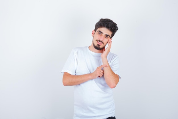 Joven sosteniendo la mano en la mejilla en camiseta y mirando feliz