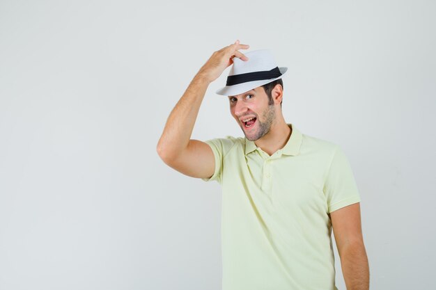 Joven sosteniendo la mano en su sombrero en camiseta y luciendo guapo