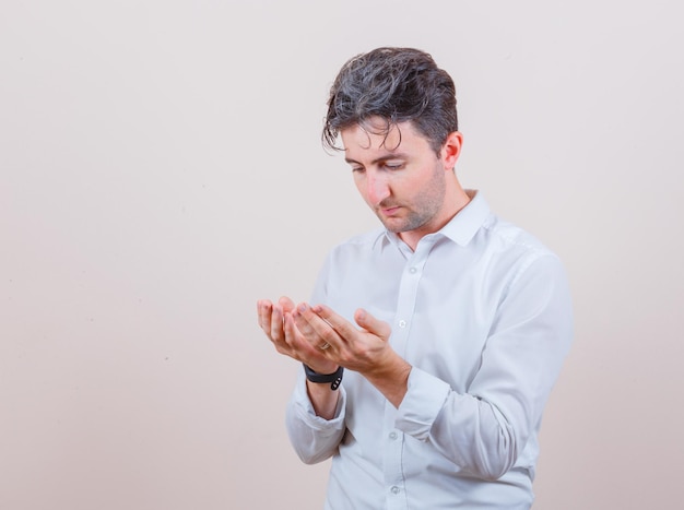 Joven sosteniendo las manos ahuecadas en gesto de oración con camisa blanca y mirando esperanzado