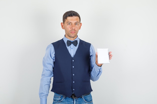 Joven sosteniendo mini notebook en traje, jeans y mirando serio