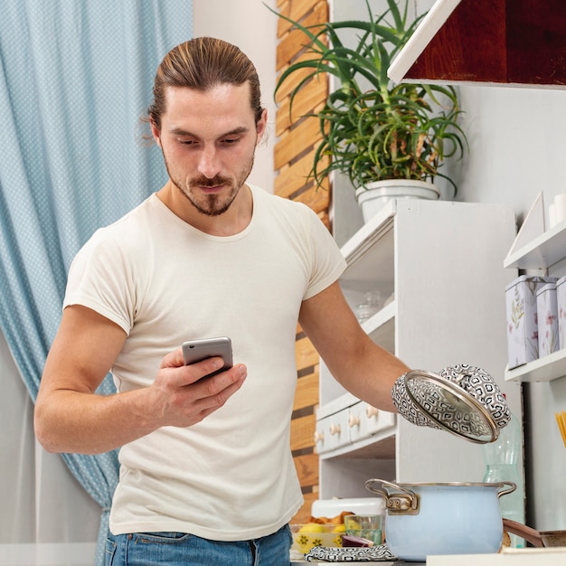 Foto gratuita joven sosteniendo una olla tapa y mirando el teléfono