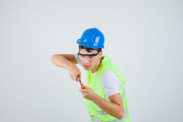 Joven sosteniendo pinzas en uniforme de construcción y mirando enfocado.