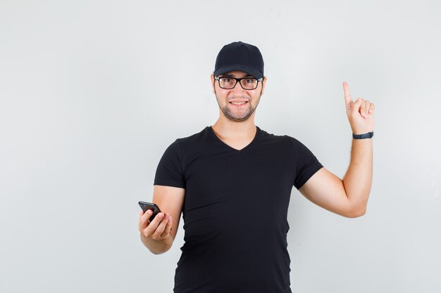 Joven sosteniendo smartphone con el dedo hacia arriba en camiseta negra