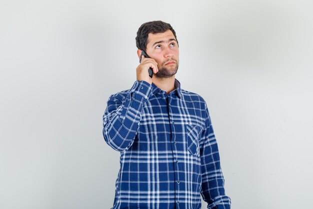 Joven sosteniendo smartphone y pensando en camisa a cuadros