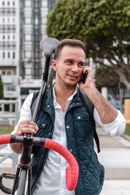 Joven sosteniendo su bicicleta y hablando por teléfono