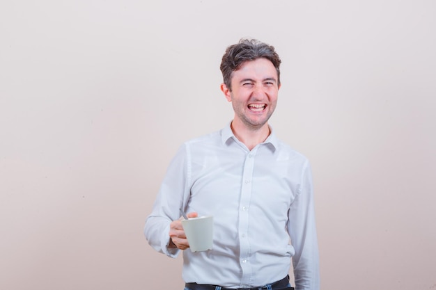 Joven sosteniendo una taza de bebida en camisa blanca, jeans y mirando feliz