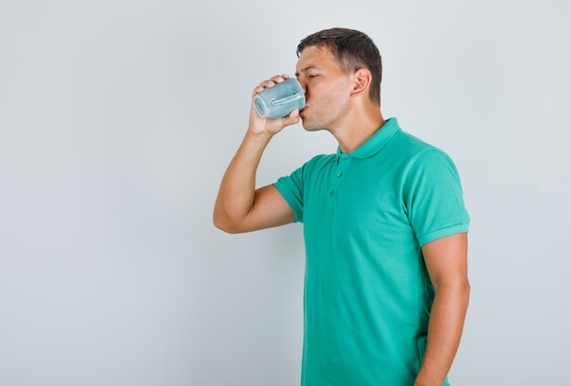 Joven sosteniendo la taza y bebiendo en camiseta verde.