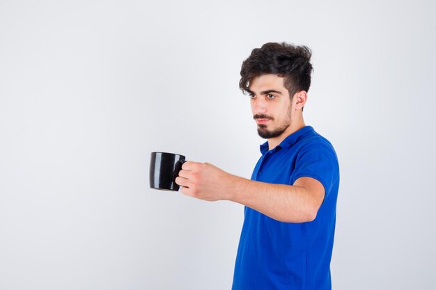 Joven sosteniendo la taza en camiseta azul y mirando serio