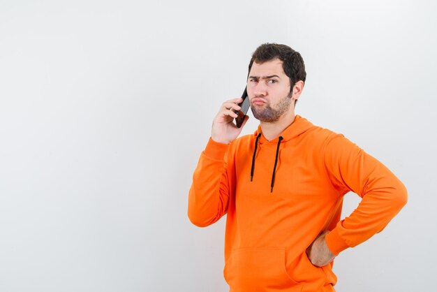 Joven sosteniendo un teléfono móvil en la mano y apoyándolo en la oreja izquierda sobre fondo blanco.