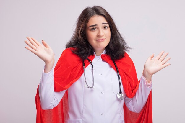 Joven superhéroe caucásica despistada vestida con uniforme médico y un estetoscopio haciendo no sé gesto
