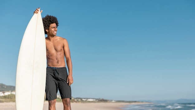Joven surfista negro mirando el océano azul