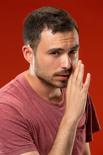 El joven susurrando un secreto detrás de su mano sobre la pared roja.