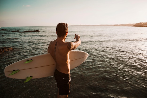 Joven con tabla de surf apuntando con el dedo