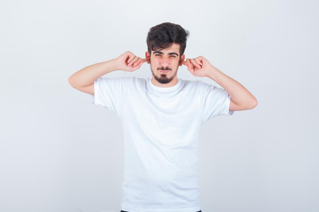 Joven tapando los oídos con los dedos en la camiseta y mirando molesto