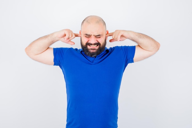 Foto gratuita joven tapándose los oídos con los dedos en camisa azul y mirando nervioso, vista frontal.