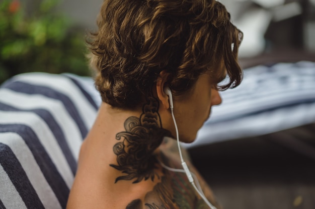 un joven tatuado con auriculares escucha música y dibuja un cuaderno.