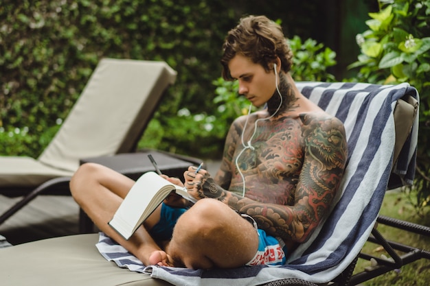 un joven tatuado con auriculares escucha música y dibuja un cuaderno.