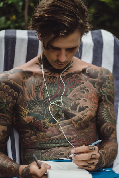 Foto gratuita un joven tatuado con auriculares escucha música y dibuja un cuaderno.