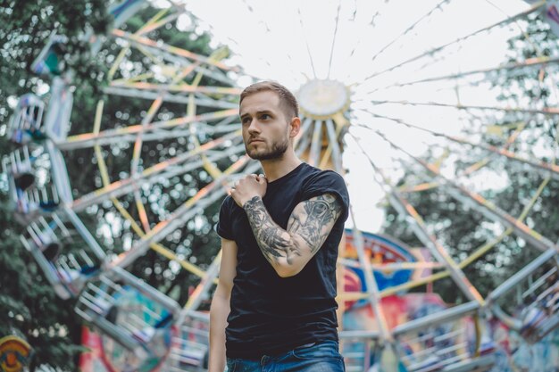 joven tatuado en un parque de atracciones en el fondo de un tiovivo