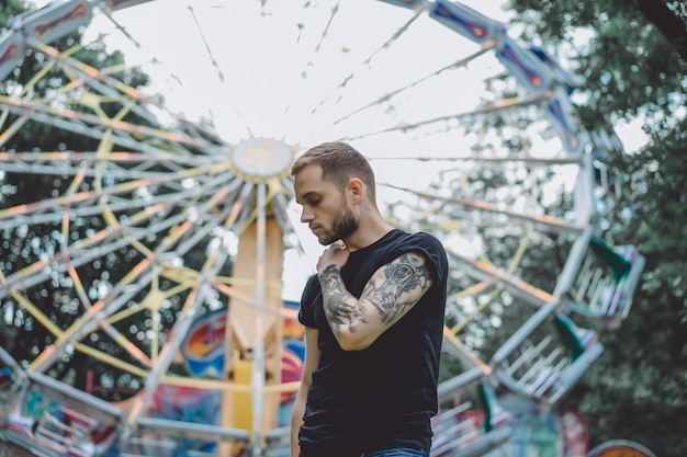 joven tatuado en un parque de atracciones en el fondo de un tiovivo