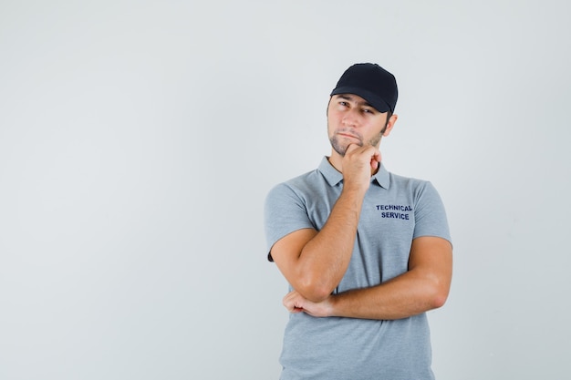 Joven técnico apoyando la barbilla en la mano con uniforme gris y mirando vacilante.