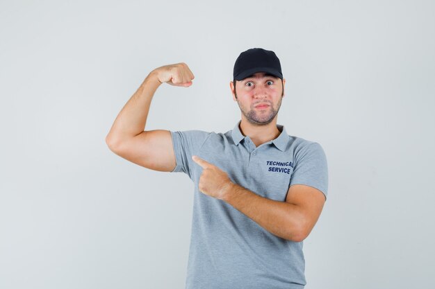 Joven técnico apuntando a los músculos del brazo en uniforme y mirando confiado.