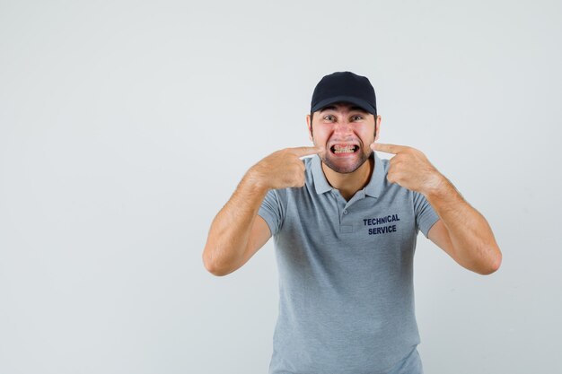 Joven técnico apuntando a sus dientes en uniforme gris.