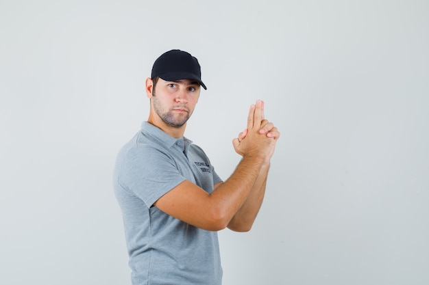 Joven técnico haciendo signo de pistola de dedo en uniforme gris y con aspecto estricto.