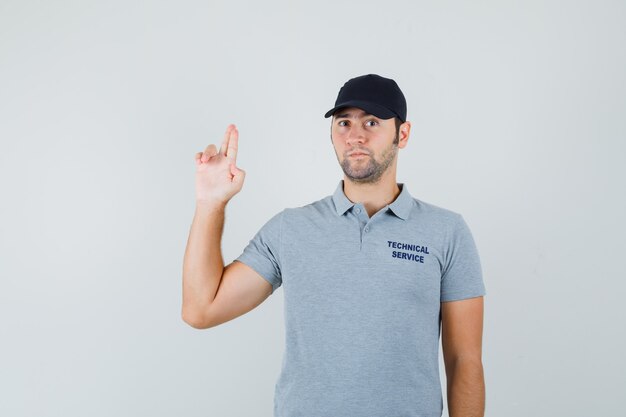 Joven técnico haciendo signo de pistola de dedo en uniforme gris y mirando pensativo.