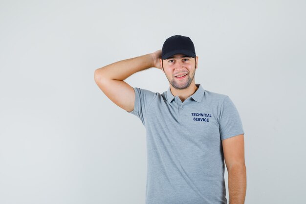 Joven técnico con la mano detrás de la cabeza en uniforme gris y elegante.