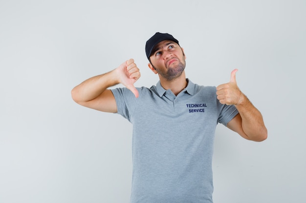 Joven técnico mostrando los pulgares hacia arriba y hacia abajo en uniforme y con aspecto indeciso.