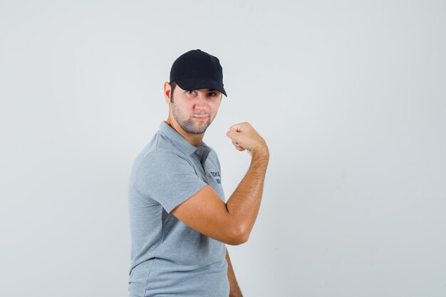 Joven técnico que muestra los músculos del brazo en uniforme gris y parece confiado.