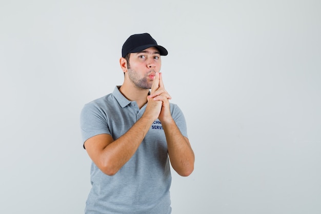 Joven técnico soplando pistola de dedo en uniforme gris y mirando confiado.