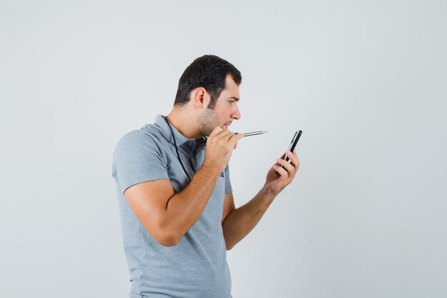 Joven técnico tratando de abrir la parte posterior de su teléfono inteligente usando un taladro en uniforme gris y mirando enfocado.