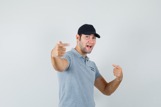 Joven técnico en uniforme gris apuntando hacia afuera y mirando juguetón.