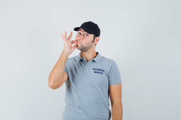 Foto gratuita joven técnico en uniforme gris mostrando gesto de cremallera y mirando ansioso.