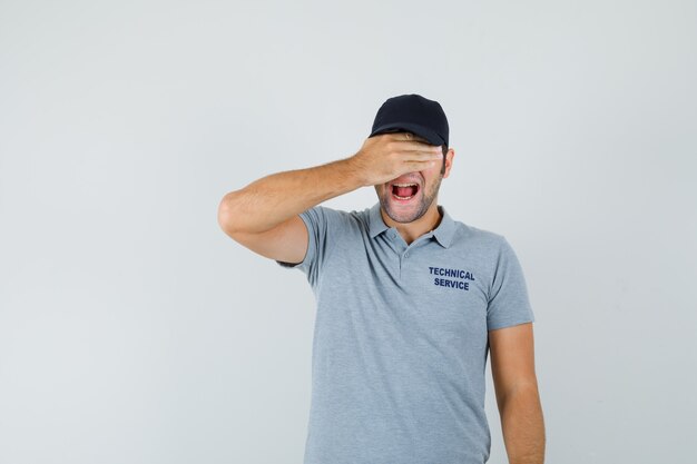 Joven técnico en uniforme gris sosteniendo la mano en los ojos y mirando emocionado.