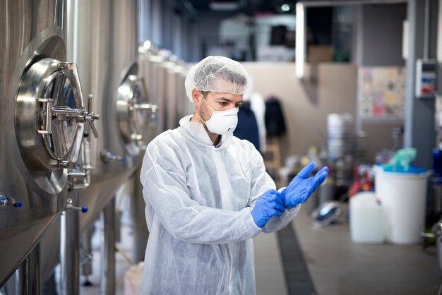 Joven tecnólogo poniéndose guantes de goma protectores en la fábrica de producción
