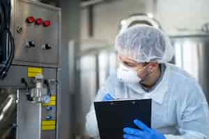 Foto gratuita joven tecnólogo en uniforme protector blanco que controla la máquina industrial en la planta de producción