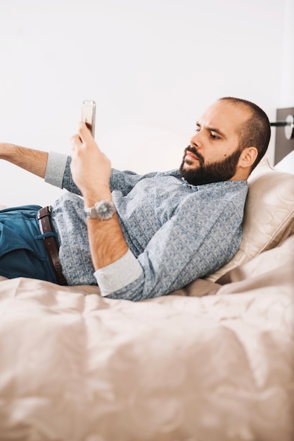 Foto gratuita joven con teléfono inteligente en la cama