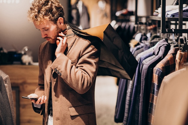 Joven en la tienda de ropa masculina hablando por teléfono