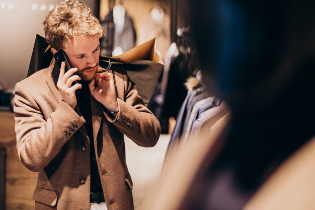 Joven en la tienda de ropa masculina hablando por teléfono