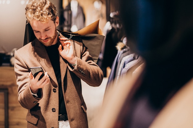 Joven en la tienda de ropa masculina hablando por teléfono