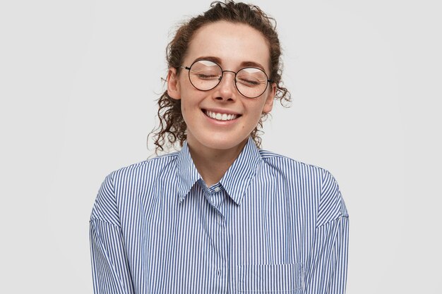 Foto gratuita la joven tímida y complacida mujer pecosa cierra los ojos, tiene una amplia sonrisa, imagina algo fantástico, tiene una expresión relajada, sueña con nuevas relaciones románticas, aislado sobre una pared blanca.